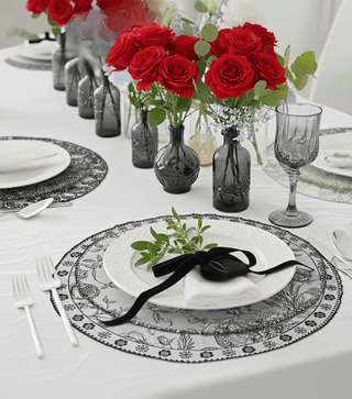 Elegant tablescape: white tablecloth, patterned placemats, red roses in gray vases, and place settings with black ribbon.