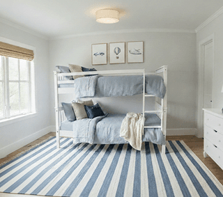 Bedroom features white bunk beds with blue linens, striped blue rug, and transportation themed wall art.