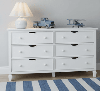 White six-drawer dresser with a blue lamp, truck, and airplane on top. Blue and white striped rug underneath.