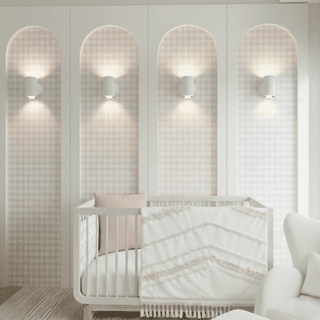 “Storkcraft crib in girls’ nursery styled with bohemian pink Sweet Jojo Designs bedding, arched accent wall panels with gingham wallpaper, and LED wall lights. Cozy and whimsical nursery design perfect for a baby girl’s room.”