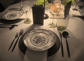 Elegant table setting with floral plates, black cutlery, glassware, and neutral tablecloth.